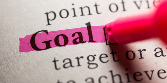 How to set realistic social media goals. A pink highlighter highlights the word "Goal" in bold in a page from a book.